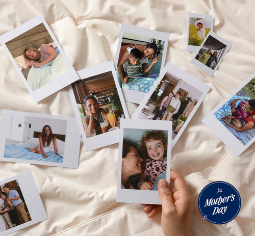 An array of Polaroid photos spread out on a silky cream-colored bedsheet. Each photo captures heartfelt moments between mothers and their children, with scenes of laughter, embraces, and shared experiences. The pictures feature diverse families and settings, from outdoor adventures to cozy indoor scenes. A round Mother's Day sticker with elegant font and a dark blue background is prominently displayed in the bottom right, adding a celebratory touch to the composition.